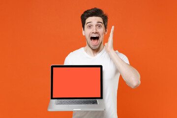 Shocked amazed screaming young man 20s wearing basic casual white t-shirt hold laptop pc computer...