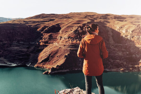 Woman in red jacket standing alone on mountain in Russia North Caucasus enjoying landscape and lake. Travel lifestyle vacations tourism outdoor trip Back view