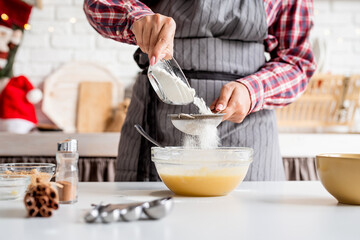 Young latin woman pouring flour to the dough cooking at the kitchen