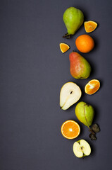 Top view of whole and pieces of oranges, pear, apples on the dark grey surface.Empty space