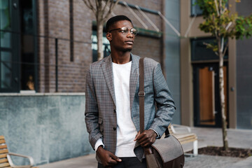 Confident african american man in eyeglasses walking with bag on street