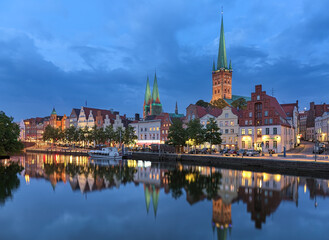 Fototapeta premium Lubeck, Germany. Evening of the Lubeck Old Town with two towers of St. Mary's Church and single tower of St. Peter's Church. View from the shore of Trave river.