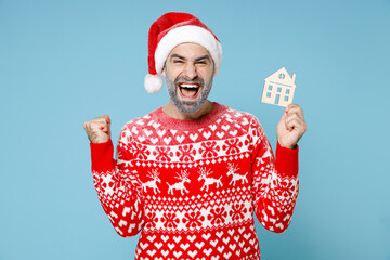 Happy Northern bearded man frozen snow face in Santa hat Christmas sweater hold house doing winner...