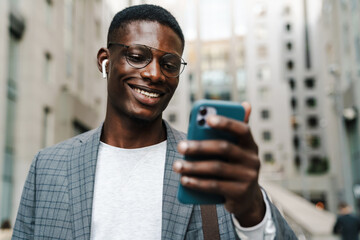 Happy african american man in earphones using mobile phone