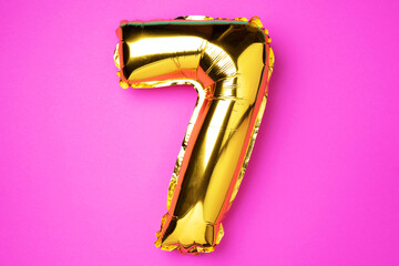 Creative layout. Golden foil balloon number and digit seven 7. Birthday greeting card. Anniversary concept. Top view. Copy space. Stylish gold numeral over pink background. Numerical digit.