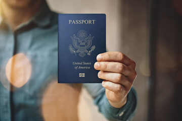 Man holding usa passport and wearing blue jeans shirt and showing blank white business card. Blurred background. Horizontal mockup