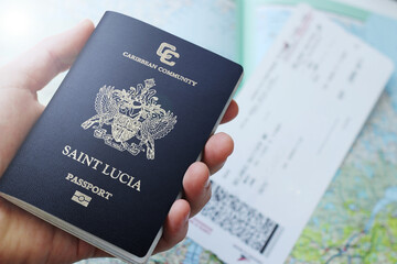 saint lucia passport in a man's hand with a plane ticket and map in the background. This image can be used to represent emigration or travelling. This image has selective focusing.