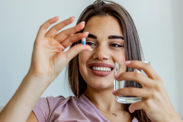 Young woman taking a daily medicine. Young female takes pill with glass of water in hand. Woman...