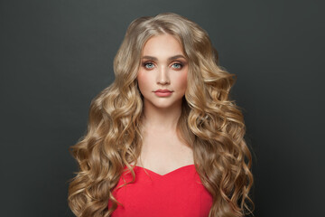 Attractive young woman celebrity with makeup and blonde curly hairstyle in red evening dress on...