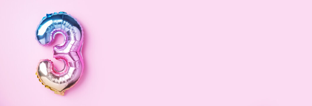 Creative layout. Rainbow foil balloon number and digit three 3. Birthday greeting card. Anniversary concept. Top view. Copy space. Stylish colored numeral over pink background. Numerical digit. - Powered by Adobe