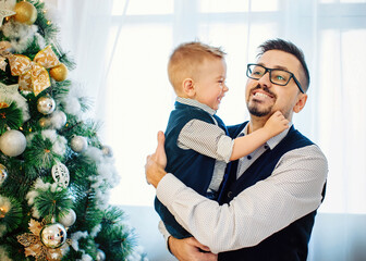Portrait of happy father and adorable kid against domestic festive backdrop with Christmas tree. Winter time and family love