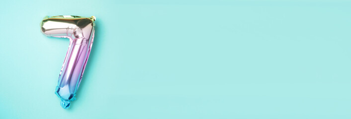 Creative layout. Rainbow foil balloon number and digit seven 7. Birthday greeting card. Anniversary concept. Top view. Copy space. Stylish colored numeral over blue background. Numerical digit.