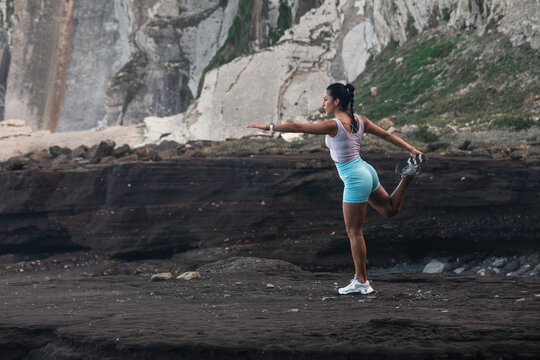 young woman stretching before exercising while looking at the horizon on the beach