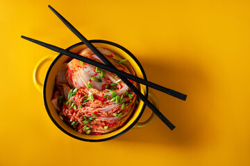 Kimchi cabbage in a bowl with chopsticks on a colored background, top view, Korean cuisine. Trend food photography