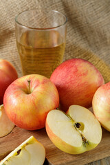 Fresh harvesting red apples and glass of cider or sparkling juice on wooden table over canvas bag.