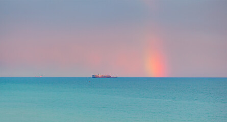 Container cargo ship with stormy sea and sky, amazing rainbow in the background
