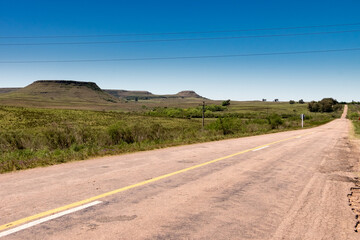 Fototapeta na wymiar A road without any cars and some hills on the background in Uruguay, next to Tacuarembó. Classic hills formations on this part of the country.