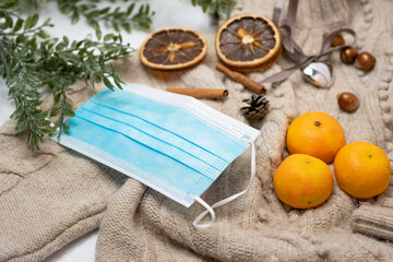 Medical mask and accessories for the New Year, a green twig, dry oranges, tangerines, a woolen sweater. Flatley on a white background.