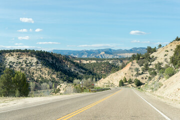 Lonely road between mountain ridges with some trees on each side of the road, somewhere in Utah, United States