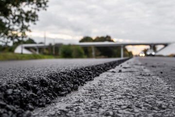 A large layer of fresh hot asphalt. Layer of asphalt raw material in a shallow depth of field. Rollers rollin fresh hot asphalt on the new road. Road construction. Construction of a new road.