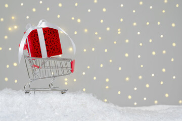 Christmas sales. Miniature trolley with Christmas gift. Warm light background 