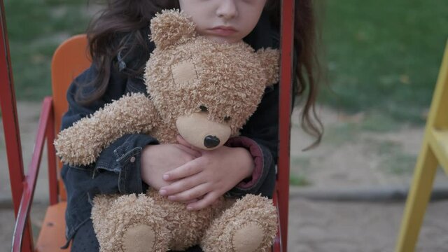 Depressed girl on the swing. A sad stressed little girl embrace her teddy bear on the swing in loneliness.