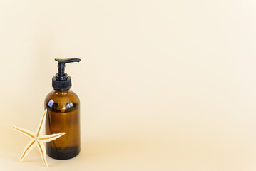 Cosmetic product in a glass bottle with a starfish on a beige background. Horizontal orientation, copy space.