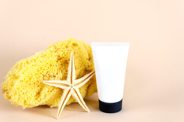 Cream in a plastic tube with a starfish and a sponge on a beige background. Mockup of a cosmetic product.