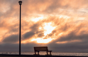A Wooden bench and street lamp with a background view of a  bright sunset