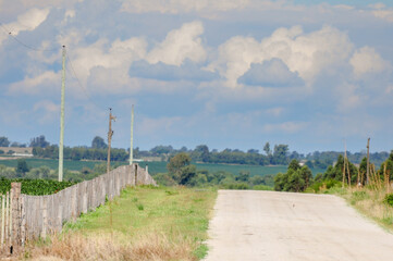 Lonely gravel road with a fence on the left side and a horizon full of stormy clouds