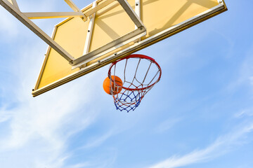 A basketball ball flies into a hoop with a net against a blue cloudy sky. Sports activities on the...
