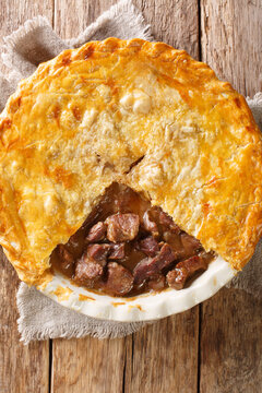 British Steak and Ale Pie is a tender pieces of steak are cooked with vegetables and English ale, then wrapped in a flaky buttery crust closeup in the dish on the table. vertical top view from above
