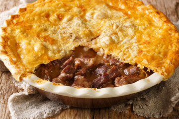 English beef steak pie with crispy puff pastry close-up in a baking dish on the table. horizontal