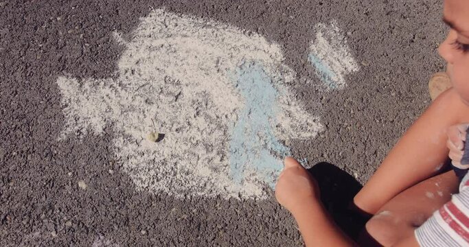 Little boy drawing on asphalt road with chalk