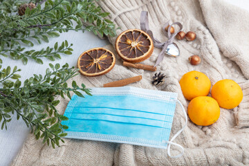 Medical mask and accessories for the New Year, a green twig, dry oranges, tangerines, a woolen sweater. Flatley on a white background.