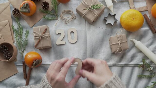 A girl lays out the wooden numbers 2021 on the table in a Christmas atmosphere, top view. Concept 2021 new year is coming. New year's natural background. Craft paper gifts with your own hands.