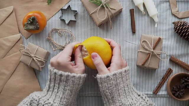 Girl cleans tangerine surrounded by Christmas gifts, Christmas tree. The concept of new year, Christmas atmosphere. Gifts made of natural materials, decorated with your own hands.
