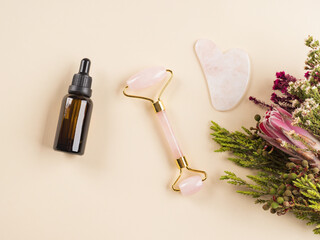 Essential oil and guasha face roller in floral frame. Natural beauty skin care products