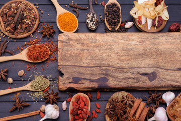 Wooden cutting board and spoons spices chili garlic salt kosher pepper on a dark wooden table. Top view with copy area