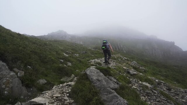 A man climbing a steep rocky mountain path into cloud, mist and fog