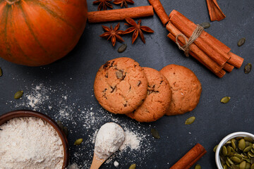 Spices, orange pumpkin, cookies and flour in bowl on black table. Autumn menu or bakery concept. Fall, home baked pastry, thanksgiving, top view