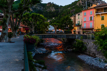 Fototapeta premium A picturesque view of a small mountain river flowing through a French medieval alpine village at dusk (Puget-Theniers, Alpes-Maritimes, Provence-Alpes-Cote-d'Azur, France)