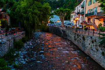 Obraz na płótnie Canvas A picturesque view of a small mountain river flowing through a French medieval alpine village at dusk (Puget-Theniers, Alpes-Maritimes, Provence-Alpes-Cote-d'Azur, France)