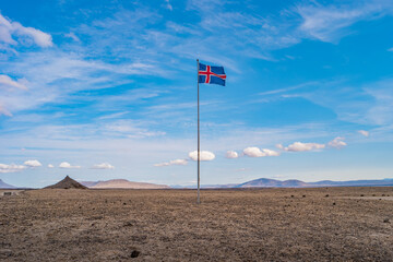 Fototapeta na wymiar Panoramic view over Icelandic landscape of the deadliest volcanic desert in Highlands, with stones and rocks thrown by volcanic eruptions and Icelandic blue with red cross flag, Iceland