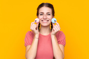 Young woman over isolated yellow background holding colorful French macarons and smiling