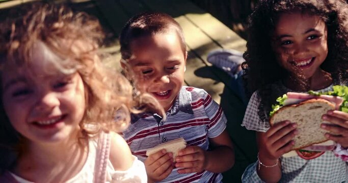 Adult playing with group of kids smiling and eating sandwiches