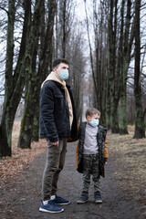 Fototapeta premium dad and son are standing in the middle of the park looking to the side, their faces are wearing medical masks as precautions, a virus epidemic, a single father