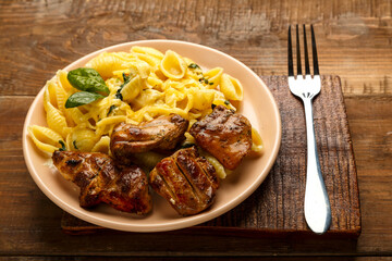 A plate of pasta in a creamy sauce with spinach and chicken on a wooden board next to a fork.