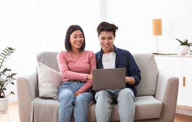 Japanese Spouses Using Laptop Sitting On Couch In Living Room