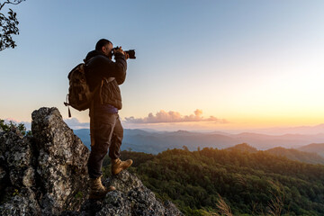 Nature photographer with backpack taking a photo on the top of mountains at sunset